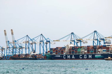 Birzebbuga, Malta - 13 Nisan 2025: Yükselen mavi konteyner vinçleri, istiflenmiş nakliye konteynerleri ve yoğun limana yanaşmış büyük bir kargo gemisi ile Malta Freeport sanayi manzarası
