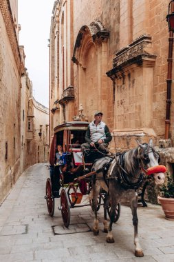 Mdina, Malta - 14 Nisan 2025: Malta mimarisinin tipik altın kireçtaşı binaları ile Mdina 'nın dar ve tarihi sokaklarında turistleri taşıyan geleneksel at arabası