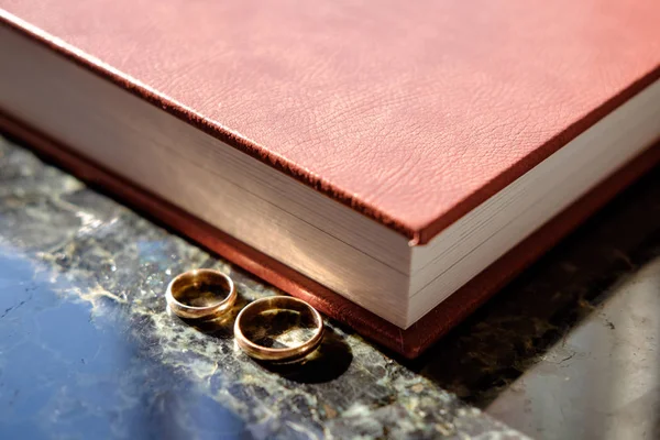 Brown leather covered wedding album with pair of wedding golden rings with reflection on labradorite surface, view from end face.