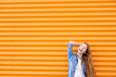 uzun saçlı Kızıl saçlı kız kot gömlek turuncu duvar gülümseme yakınındaki kapalı gözlerle. Mutluluk