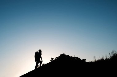 Gezgin tepelerde mavi gökyüzü arka plan üzerinde hiking sırt çantası ile silüeti