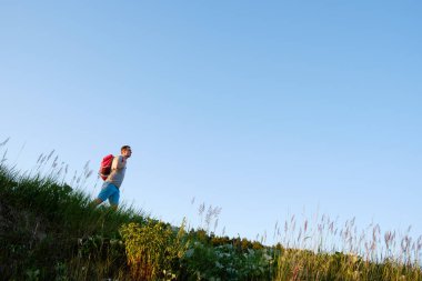 Gezgin turuncu sırt çantası ile yürümek tepeler mavi gökyüzü arka plan üzerinde