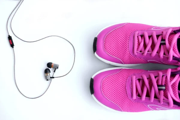 Concept run. Pink running shoes for women and headphones on a white background. Top view.