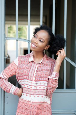 Metal geçidin yakınlarında poz ve gülümseyen süsleme elbiseli siyah afro kız