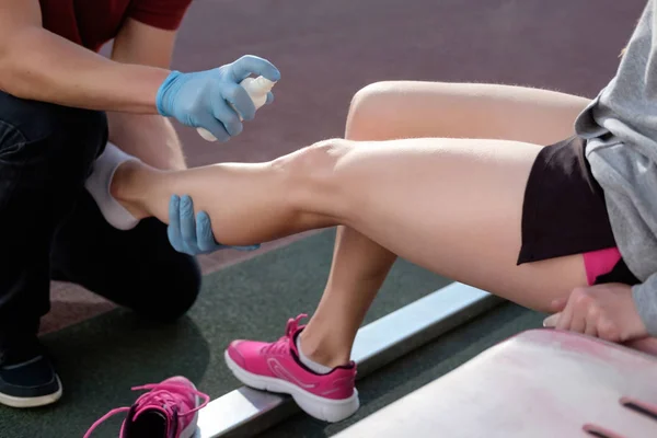 Sports doctor treating injured sportman\'s knee. Sport medicine in action. Injured tenis player\'s or athlete leg is anesthetizing by sport doctor using freezing spray.