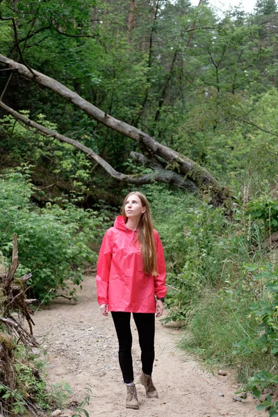 Genç Kızıl saçlı kadın, pembe yağmurluk renksizdir yaz bulutlu ormanda yayılıyor. Kavram seyahat.