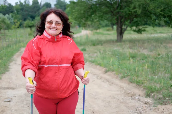 Nordic walking - woman working out outdoor. Senior woman in red raincoat with Scandinavian sticks.