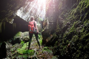 Turuncu seyahat sırt çantası ve lightern olan kadın eski kale mağara, arka görünümünden araştırıyor