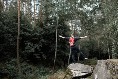 Genç adam sırt çantası üst kısmında rock ormandaki tek ayak üzerinde dengeleme hiking portakal ile