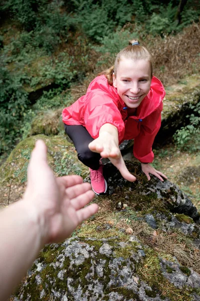 Young woman takes her companion\'s hand of help during hiking the rocks in forest. Travel concept. Mutual aid concept.
