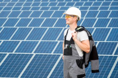 Elektrik işçi ya da mühendis beyaz fıçı, koruyucu sarı gözlük ve güneş panelleri field yakınındaki gri kıyafet stadnding. Sıcak güneşli yaz hava. Alternatif enerji türleri. Yenilenebilir ve temiz enerji, teknoloji kavramı. Kopya alanı.