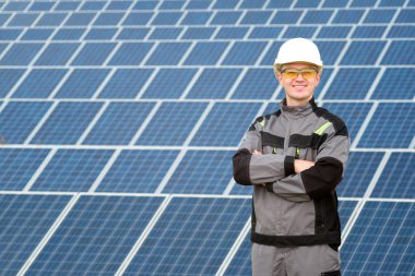 Genç bir mühendis veya alt beyaz fıçı, koruyucu sarı gözlük ve güneş panelleri field yakınındaki gri kıyafet stadnding portresi. Sıcak güneşli yaz hava. Alternatif enerji. Yenilenebilir ve temiz enerji, teknoloji kavramı. Kopya alanı.