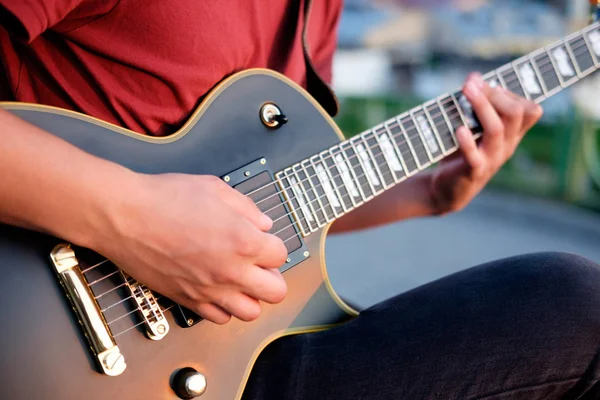 hands of guitarist playing electric guitar outdoors, evening