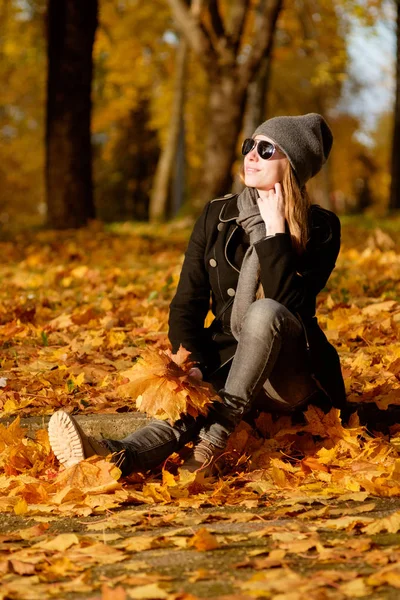 サングラスの黄色のカエデ Leves のヒープに座っていると笑顔で赤毛の女の子 秋の天気晴れ — ストック写真