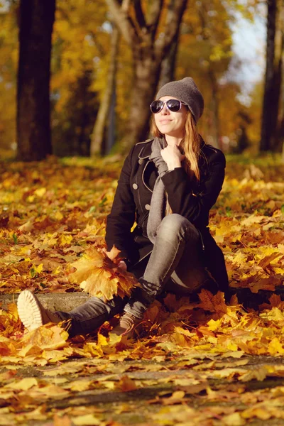 サングラスの黄色のカエデ Leves のヒープに座っていると笑顔で赤毛の女の子 秋の天気晴れ — ストック写真