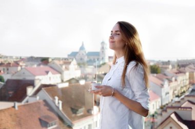 Beyaz gömlekli ise açık hava yer ya da gözlem güvertesinde kahve içmek kapalı gözlü genç çekici kız. Arka plan üzerinde eski şehir.