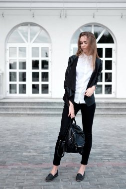 Şık güzel genç kadın moda siyah deri ceket, beyaz gömlek, siyah pantolon siyah sırt çantası elinde. 