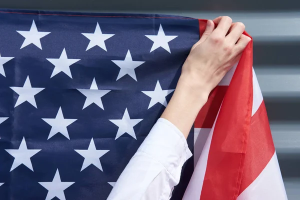 Hand of woman, hanging usa flag on a grey wall, 4th july concept