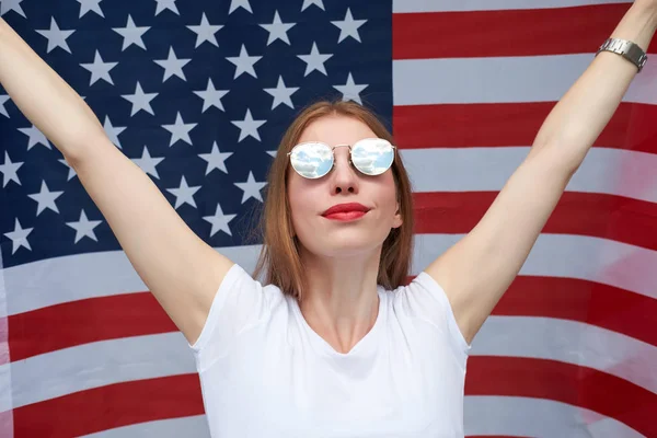 戴在美国国旗上方的太阳镜中的年轻红发女子 — 图库照片