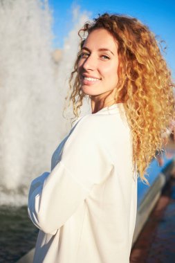Genç redhead kıvırcık beyaz gülümseyen kız, suni beyaz elbise, Çeşme standları