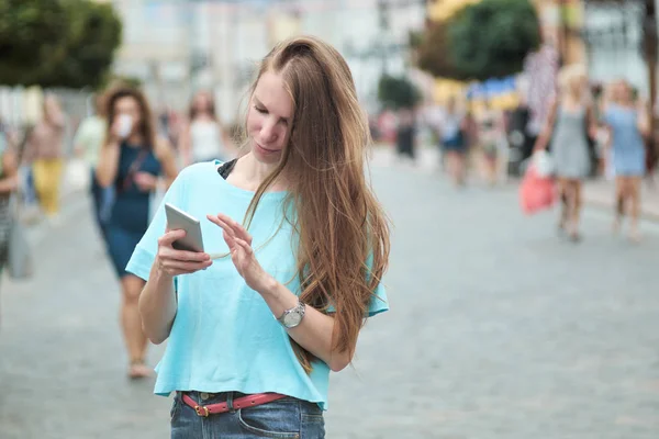 Young skinny redhead girl has a walk in the street and typing something on her smartphone.