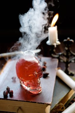 Magic and wizardry concept. Set of sorcery book, magic potion in skull shaped bottle and candles on table. Alchemy concept. Halloween concept.