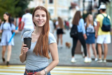 Kızıl saçlı kız kahve ile gülümseyen beyaz bir yürüyüş sokakta bulunmaktadır.