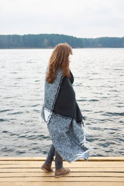 Kızıl saçlı kadın sonbaharda göl iskelede duran ve uzak seyir ekose sarılmış. Sonbahar bulutlu kötü hava.