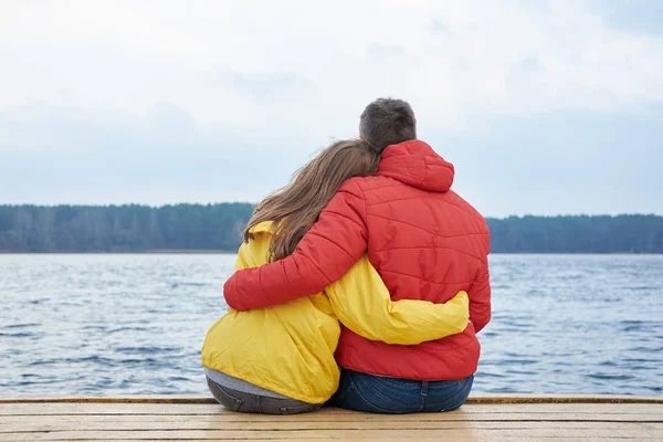 Pareja Blanca Con Chaquetas Amarillas Rojas Sentadas Abrazándose Muelle Cerca — Foto de Stock