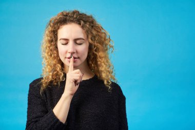 İşaret parmağı dudaklar yakınındaki mavi bir arka plan üzerinde tutan kapalı gözlü genç çekici Kızıl saçlı kız. Kadın sessizlik koymak istiyorsun. Kopya alanı. 