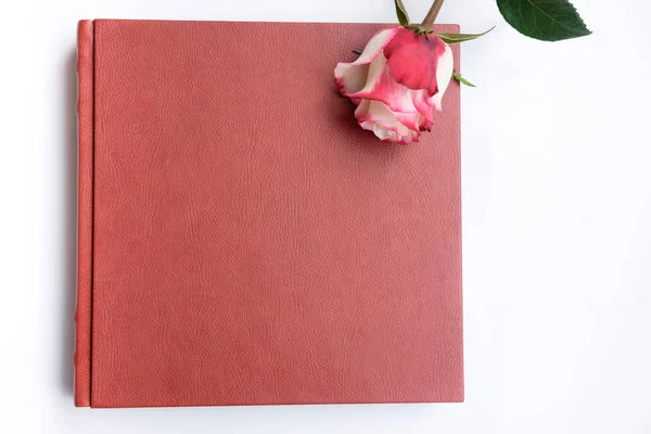 Red leather covered wedding book or wedding album lie on white background, one rose lie on weding book. Top view.