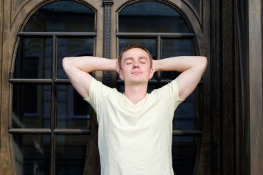 Yakışıklı genç vintage kapı yakınında kapalı gözler ile ayakta adam ve anın tadını çıkarın. Portre. Kentsel arka plan. Açık. 