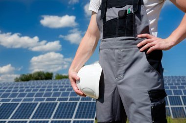 Güneş panelleri mühendis veya gri kıyafet beyaz koruyucu fıçı holding işçi, el kapatın, güneş paneli alanı ve gökyüzü arka plan. Sıcak güneşli yaz hava. Uzay kopyalayın. Yenilenebilir ve temiz enerji, teknoloji kavramı.