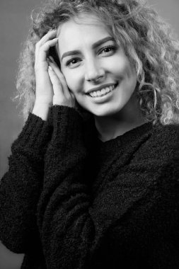 Tek renkli çekici gülümseyen neşeli kıvırcık kız portresi siyah kazak giymiş. Stüdyo vurdu.