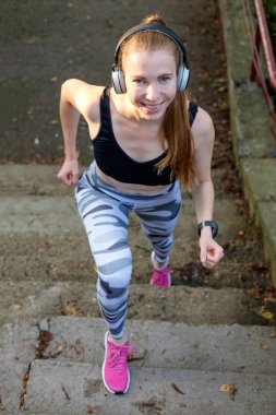 Genç çekici neşeli ince sportif kız merdivenlerden yukarı çalışır ve müzik dinliyor. Sağlıklı spor yaşam tarzı. Fitness ve egzersiz açık 