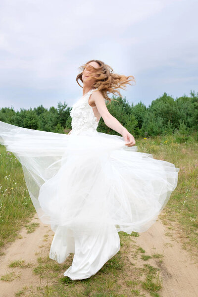 Young attractive redhead bride in stylish white wedding dress spin around. Outdoor.