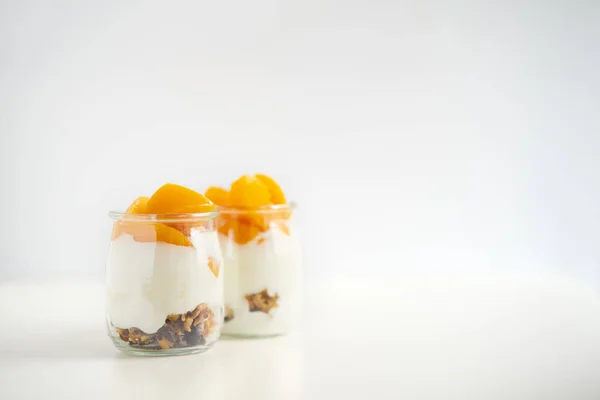Банки греческого йогурта с мюсли и консервированные абрикосы на белом "Б" — стоковое фото