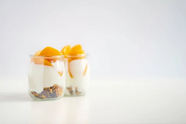 Пара стеклянных банок греческого йогурта с мюсли и консервированным априкатом — стоковое фото