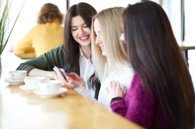 Caf içinde oturan smartphone cep telefonu ile fotoğraf izlerken gülümseyen kız