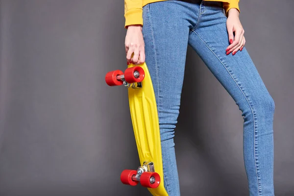 Menina vestindo blusa amarela e jeans azul segurando skatebo amarelo — Fotografia de Stock