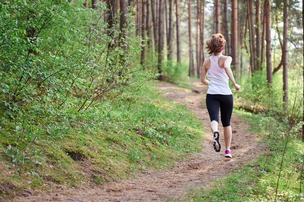 Atletische jonge vrouw in roze sneakers lopen in Spring forest — Stockfoto