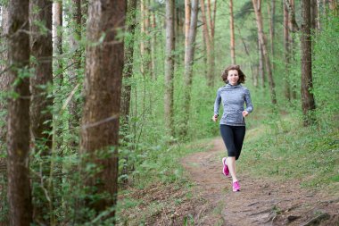 Pembe spor ayakkabılı atletik genç kadın bahar ormanında koşuyor