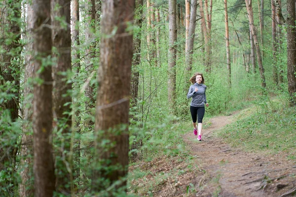 ผู้หญิงสาวนักกีฬาในรองเท้าผ้าใบสีชมพูวิ่งในป่าฤดูใบไม้ผลิ — ภาพถ่ายสต็อก