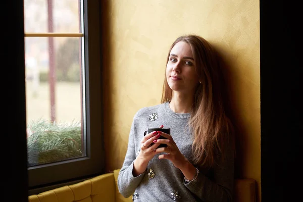 Fiatal csinos lány hosszú haj iszik kávét vagy teát a — Stock Fotó