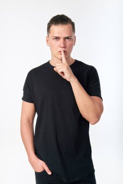 Genç, çekici, ciddi bir adam, işaret parmağını dudaklarında tutuyor.