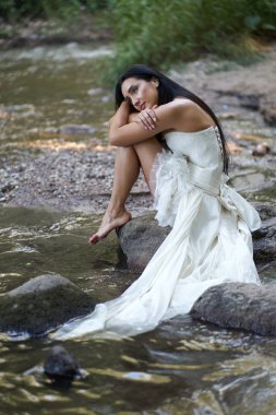 Genç güzel biraz üzgün esmer kadın beyaz gelinlik oturup