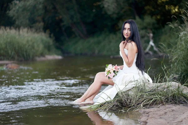 Jonge mooie brunette vrouw in witte trouwjurk zittend op th — Stockfoto