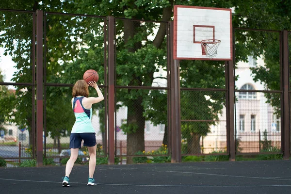 Руда худа дівчина кидає м'яч у баскетбол на відкритому повітрі — стокове фото