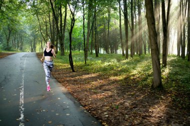 Atletik genç kız güneşli sabah parkta veya ormanda çalışan siyah üst ve trendy tozluk giyiyor. Doğru sabah. Yaz zamanı. Çalışma konsepti. Sağlık kavramı. Fitness konsepti. 