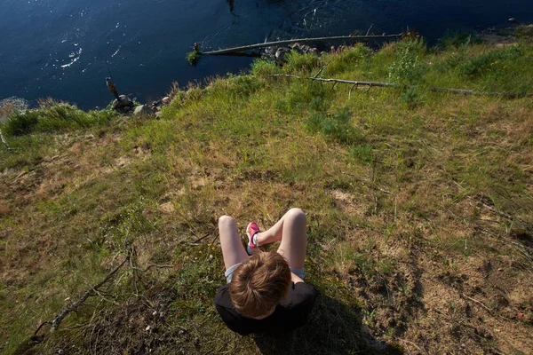 Joven chica caucásica sentada en un acantilado sobre el río bosque y e — Foto de Stock
